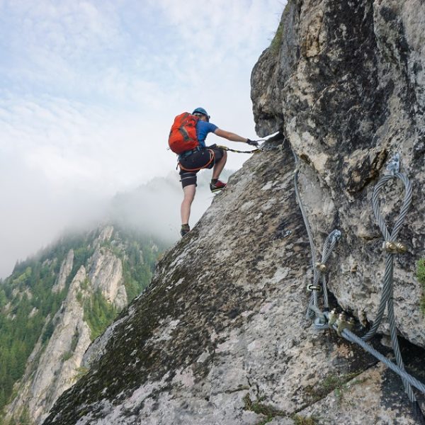 A stunning shot of a young man climbing up a cliff on a cold and foggy day